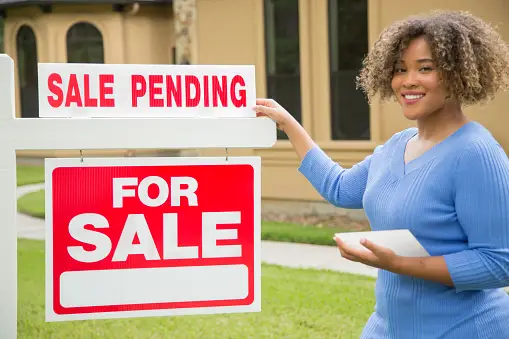 A real estate agent smiling and standing in front of a house